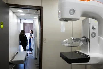 A mammography machine in the foreground at a clinic office with a doctor speaking with a patient in the background