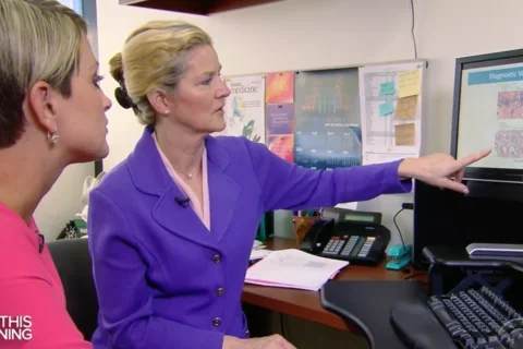 Dr. Elmore sitting at desk and pointing to a computer screen showing breast cancer biopsies