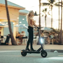 A woman rides an electric scooter on a street at sunset.