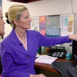 Dr. Elmore sitting at desk and pointing to a computer screen showing breast cancer biopsies