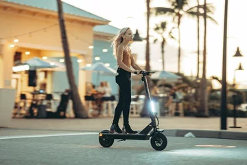 A woman rides an electric scooter on a street at sunset.