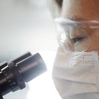 A researcher wearing protective glasses looks into a microscope.